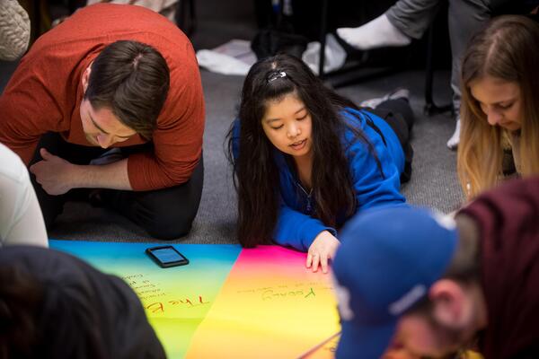 Students write on large rainbow pieces of paper.