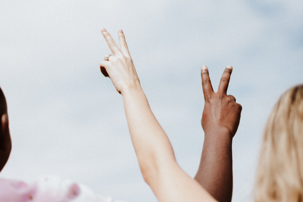 A white hand and a black hand extend into the sky holding up a peace symbol.
